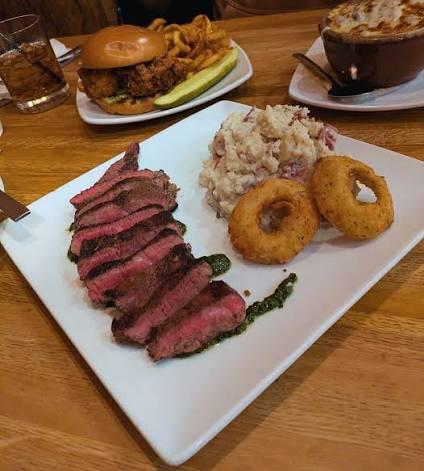 Sliced dry-aged steak with onion rings and potato salad